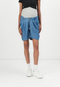 Denim maternity shorts in light blue, featuring an elastic waistband and pockets, above-the-knee length, paired with white sneakers.