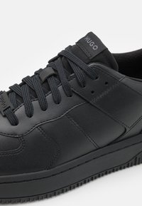 Sneaker in pelle nera con tomaia texturizzata, punta rotonda, suola in gomma spessa e lacci piatti. Presenta un marchio discreto sulla linguetta.