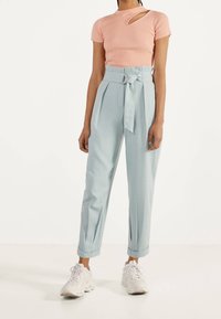 Meruňkový žebrovaný top s výstřihem, spojený s vysoce střiženými světle modrými kalhotami v kostkovaném vzoru se zavazováním vpředu a širokými nohavicemi. Bílé tenisky.