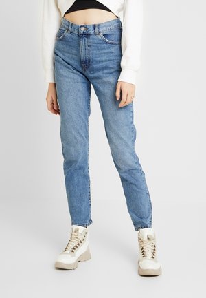 Jeans blu chiaro a vita alta con taglio dritto, realizzati in denim, abbinati a stivali color crema con lacci e suola spessa.
