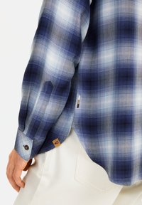 Blauw-wit geruite blouse met lange mouwen van textuurstof. Voorzien van knopen op de manchetten en een geweven label nabij de zoom.