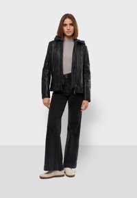 Crna kožna jakna s kapuljačom, uskog kroja, s zatvaranjem na patentni zatvarač, nosi se preko sivo rebrastog topa. Tamne široke traperice i svijetle tenisice upotpunjuju odjeću.