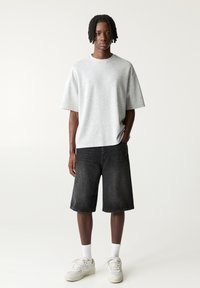Felpa grigia a maniche corte, vestibilità ampia. Abbinate a pantaloni corti in denim grigio scuro, che terminano sopra il ginocchio. Sneakers bianche e calzini completano il look.