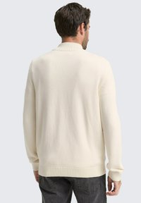 Cremefarbener, gerippter Strickpullover mit hohem Kragen und entspannter Passform; verfügt über lange Ärmel und ein einfaches, strukturiertes Design.