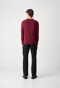 Burgunderrød genser med lange ermer, rund hals og ribbestrikket kant, kombinert med svarte rette jeans og mørkt fottøy. Enkelt, udekorerte design.