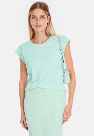 Mint green, short-sleeve t-shirt with a round neckline, paired with a knitted mint skirt. A small matching handbag is worn over the shoulder.