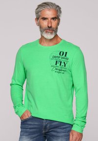 Maglietta a maniche lunghe verde lime con collo rotondo, caratterizzata da una stampa grafica nera sul petto e una vestibilità comoda, abbinata a jeans blu.