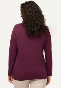 Halenka s dlouhým rukávem v tmavě fialové barvě, s kulatým výstřihem, volným střihem a měkkou, texturovanou tkaninou. Bez viditelných vzorů nebo ozdob.