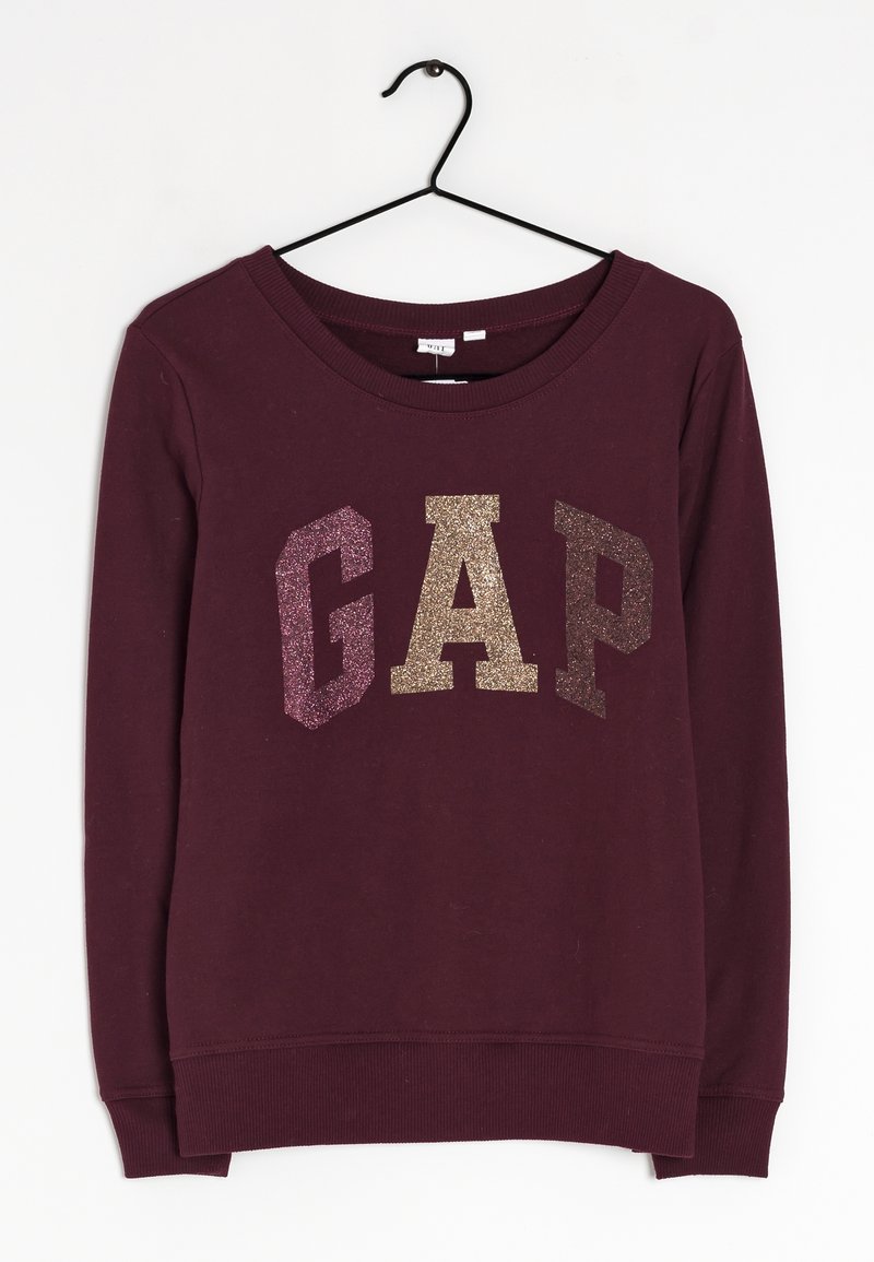 Sudadera de color púrpura oscuro con letras brillantes "GAP" en rosa, oro y marrón, colgando de una percha negra sobre un fondo blanco.
