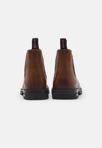Bottines Chelsea en cuir marron avec des panneaux élastiques sur les côtés, semelles en caoutchouc noir et languettes en tissu. Fini lisse et design à bout arrondi.