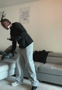 Person saugt ein hellgraues Sofa in einem Wohnzimmer mit zwei gerahmten inspirierenden Postern an der Wand.