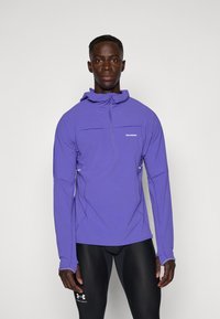 Lila lättvikts-pullover med halv dragkedja, med en huva och kontrasterande sömmar. Tillverkad av ventilerande material, idealisk för utomhusaktiviteter.