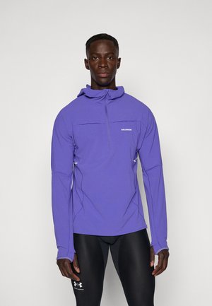 Kerge lillakate pullover poole tõmblukuga, kapuutsiga ja kontrastsete õmblustega. Valmistatud hingavast materjalist, ideaalne välitegevuseks.