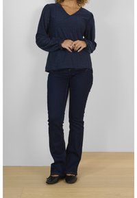 Haut bleu marine à manches longues avec un col en V, présentant des motifs texturés. Associé à un jean évasé en denim foncé et des chaussures plates noires.