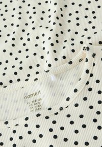 Jasnokremowa tkanina w czarne groszki; faktura prążkowana; okrągły dekolt z obszytym brzegiem; widoczna metka ubrania z informacjami o rozmiarze i pielęgnacji.