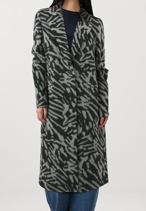 Pitkä musta- ja harmaakuosinen takki, jossa leveät kaulukset, kaksi nappia ja sivutaskut, pidetty tumman yläosan ja sinisten farkkujen päällä.