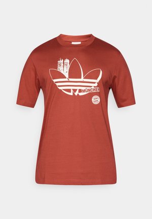 Sarkans kokvilnas T-krekls ar baltu Adidas logotipa, Minhenes panorāmas un Baijeras Minhenes emblēmas grafiku priekšpusē. Īsas piedurknes.