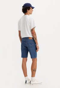 Denim shorts in dark blue, featuring a classic five-pocket design and leather logo patch at the back. Paired with a white t-shirt and sneakers.