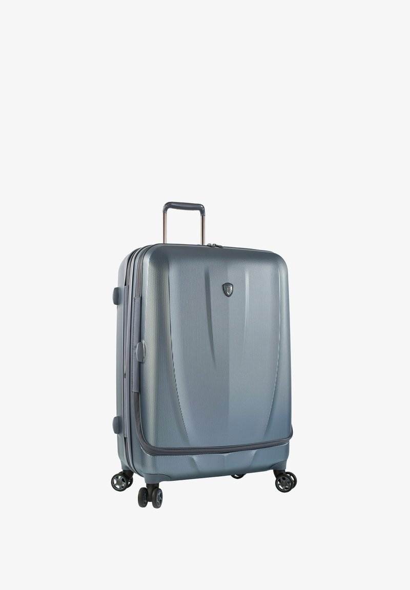 Valise à coque rigide de couleur gris métallique avec une finition texturée. Dispose d'une poignée télescopique et de quatre doubles roues pour une meilleure maniabilité.