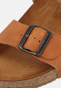 Brown leather sandal with a wide strap, a metal buckle, and a textured cork footbed. Inner side features a soft, suede-like texture.