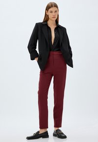 Zwarte blazer over een zwart overhemd met knopen, gecombineerd met bordeauxrode broeken en zwarte loafers. Soepele texturen en een op maat gemaakte pasvorm, minimalistisch ontwerp.