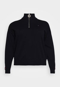 Pull-over noir avec col montant et fermeture éclair argentée à quart de tour. Il présente un petit logo sur la poitrine et des poignets côtelés.