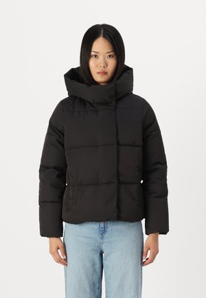 Zwarte pufferjack met een hoge hals en een vierkante pasvorm, met een gladde textuur en zichtbare naadlijnen, gedragen over lichte jeans.