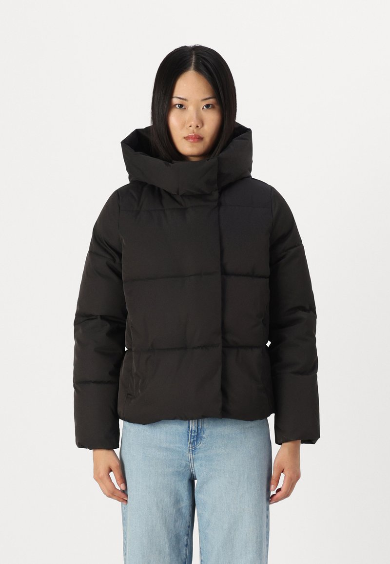 Zwarte pufferjack met een hoge hals en een vierkante pasvorm, met een gladde textuur en zichtbare naadlijnen, gedragen over lichte jeans.