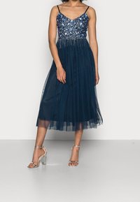 Vestido de noche azul marino con cuerpo de cuentas, tirantes finos y falda de tul. Acompañado de sandalias plateadas de tacón.