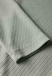 Närbild av ljusgrön ribbad tyg med vikta ärmar som visar synliga s ömmar och strukturerade vertikala linjer.