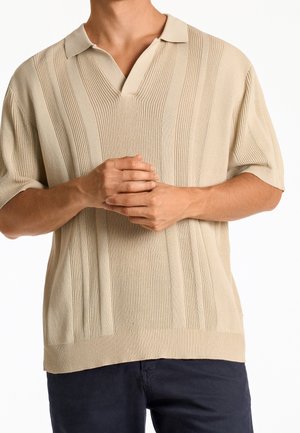 Beige kortärmad polo t-shirt med vertikal ribbad textur, V-krage och avslappnad passform. Positionerad mot en enfärgad bakgrund.