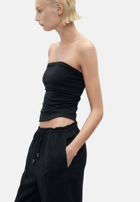 Black strapless top made of smooth fabric, paired with loose black pants featuring an elastic waistband and drawstring.