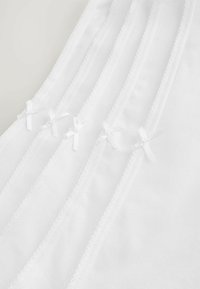 Wit katoenen kledingstuk met meerdere delicate kantafwerkingen en kleine witte strikjes, gerangschikt in horizontale lijnen. Zachte textuur en uniforme kleur.