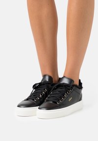 Czarne skórzane sneakersy z białą gumową podeszwą, puszystym wyściółką, złotymi oczkami i czarnymi sznurowadłami. Posiadają logo marki z boku.