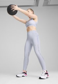 Ljusgrå träningsoutfit bestående av en sport-bh och högmidjade leggings med meshpaneler. Svart gummiboll hålls ovanför huvudet.