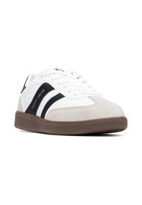 Sneaker bianca con accenti neri e grigi chiari, punta in suede, suola piatta in gomma marrone, occhielli in metallo e branding dorato "TEDDY SMITH".