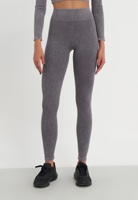 Leggings grigi con costine, vita alta, design aderente e lavorazione a maglia testurizzata. Indossati con scarpe sportive nere.