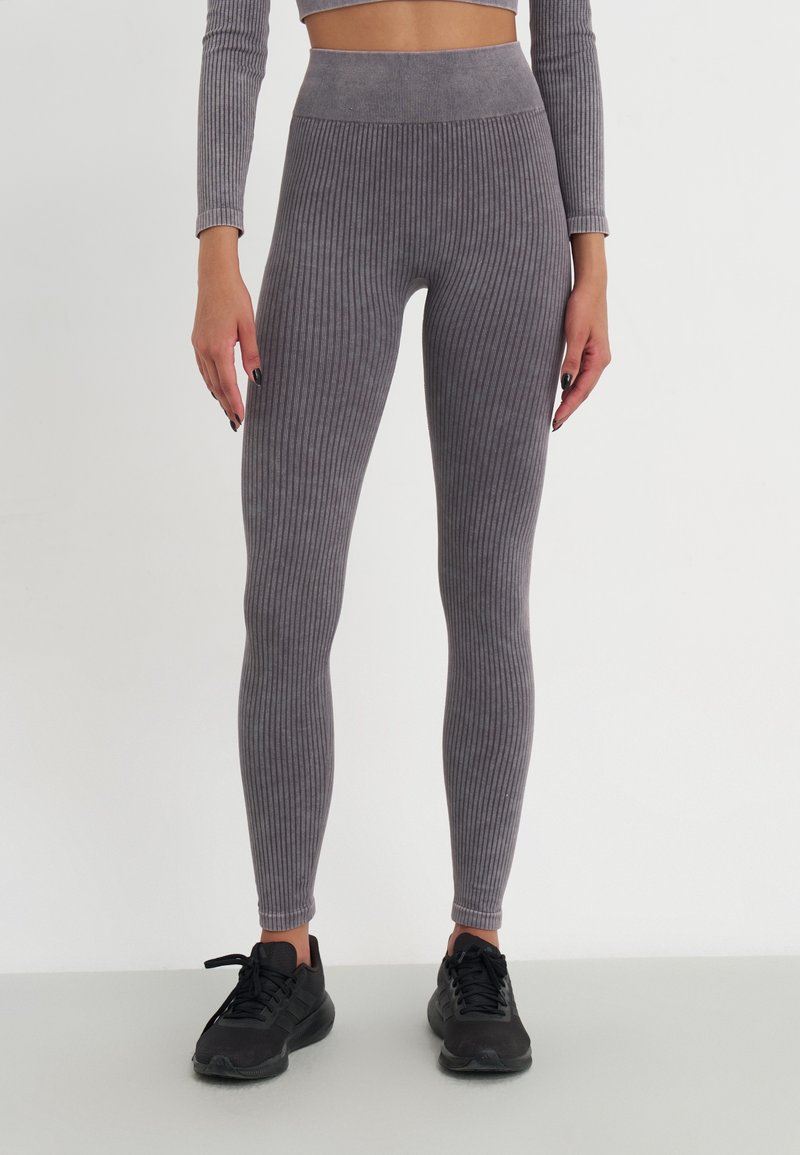 Leggings grigi con costine, vita alta, design aderente e lavorazione a maglia testurizzata. Indossati con scarpe sportive nere.