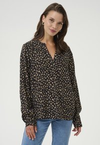 Blouse noire avec imprimé léopard dans des teintes de beige et de marron. Elle présente une coupe ample, des manches longues et un col en V. Texture de tissu lisse.
