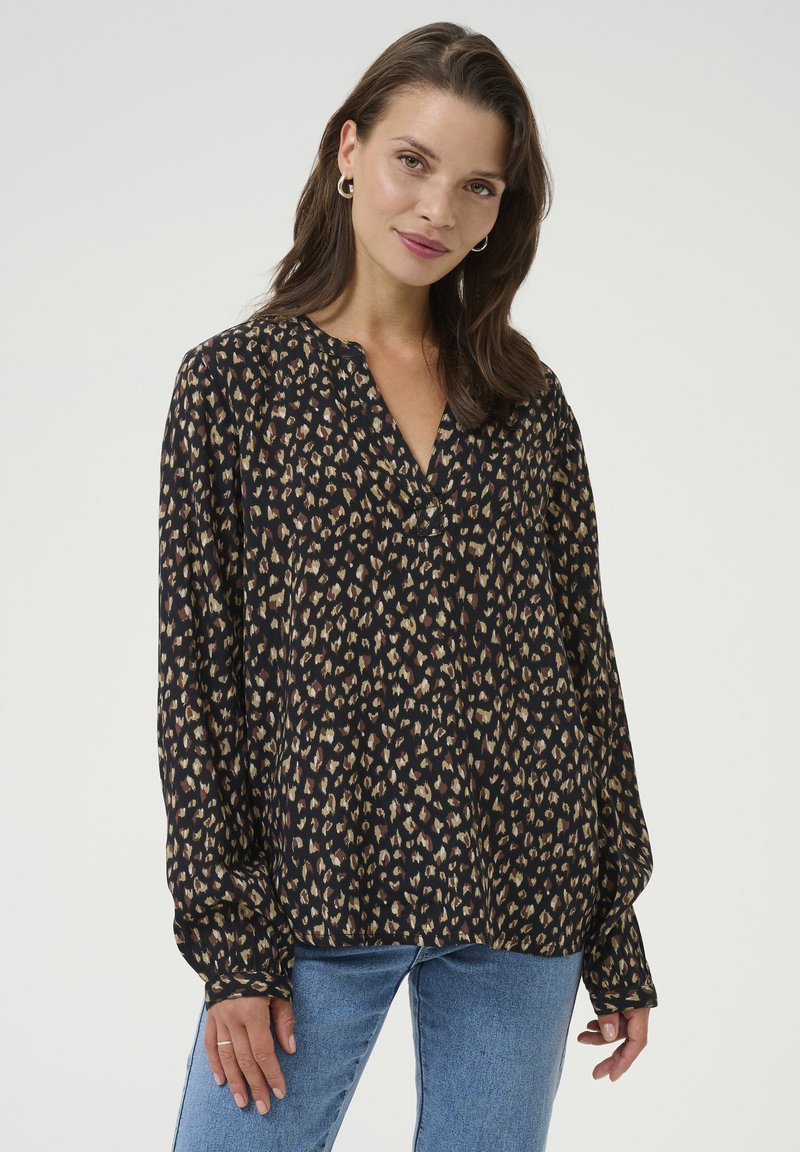 Blouse noire avec imprimé léopard dans des teintes de beige et de marron. Elle présente une coupe ample, des manches longues et un col en V. Texture de tissu lisse.