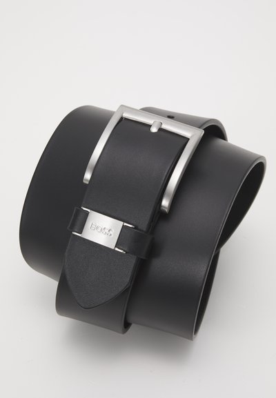 Cinturón de cuero negro con una hebilla de metal plateado, con forma rectangular y un detalle de logo. Textura suave y diseño sencillo.