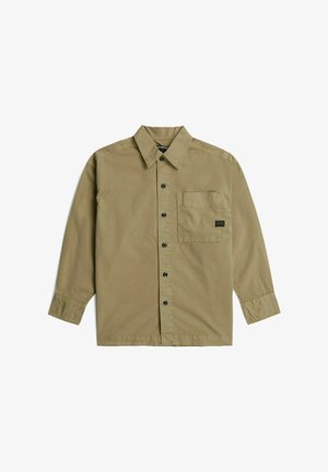 Chemise beige à manches longues, boutonnée, avec col et poche poitrine comportant une petite étiquette noire sur fond blanc.