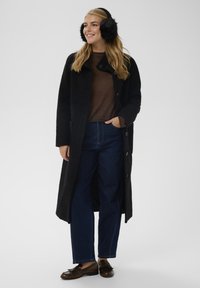 Dug kaput crne boje s teksturiranom tkaninom, ispod smeđi džemper, plave traperice i smeđe mokasinke. Ima crne krznene štitnike za uši.