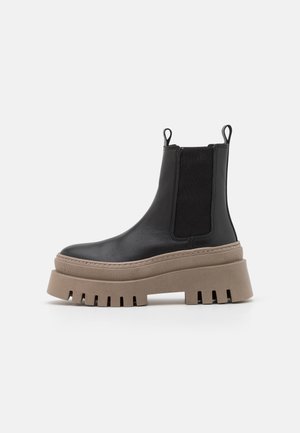 Bota de cuero negro hasta el tobillo con laterales elásticos, punta redondeada y una suela plataforma beige gruesa con detalles recortados.
