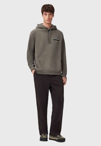 Bluza z kapturem w kolorze oliwkowej zieleni, wykonana z bawełny, z przednią kieszenią i detalem z logo. Połączona z czarnymi spodniami i sneakersami na masywnej podeszwie.