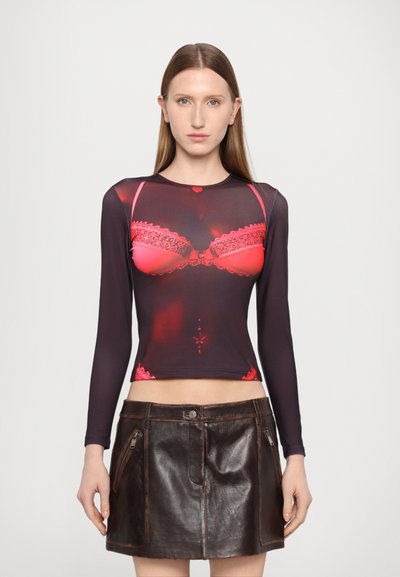 Un haut à manches longues en tissu noir transparent avec un imprimé de soutien-gorge en dentelle rouge. Associé à une mini jupe en cuir marron taille haute avec des zips.