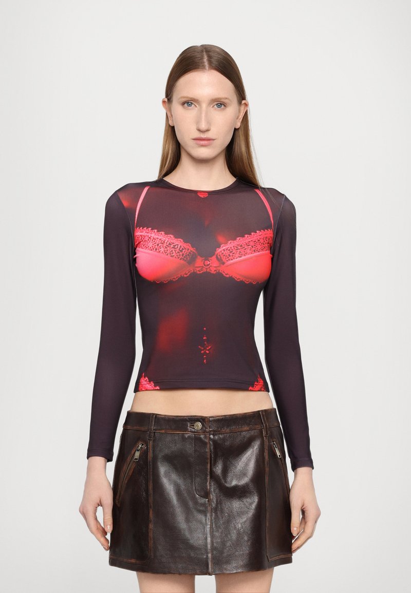Long-sleeve top features a sheer black fabric with a red lace bra print. Paired with a high-waisted, brown leather mini skirt with zippers.