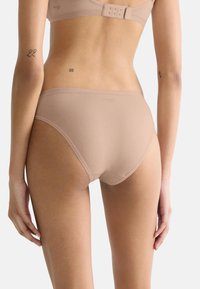 Beige naadloze damesonderbroek met een gladde textuur, gematigde dekking en een subtiele logo nabij de tailleband, gezien van de achterkant.