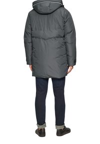 Graue gepolsterte Jacke mit Kapuze, langer Schnitt, elastischen Bündchen und einem dezenten kontrastierenden Streifen entlang des Kragens. Getragen über dunklen Jeans.
