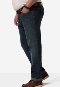 Jeans in denim blu scuro con un design a gamba dritta, tasche frontali visibili e una texture liscia. Abbinati a scarpe in pelle marrone.